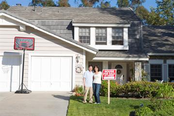 A couple standing in front of house with a for sale sign